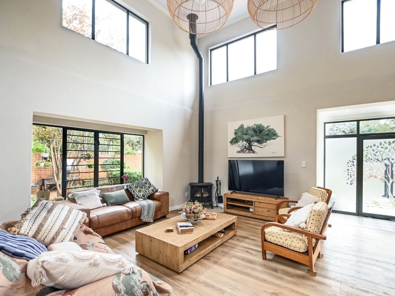 Spacious double-volume living room featuring a modern freestanding fireplace, large windows for natural light, and direct access to the garden through sliding doors.