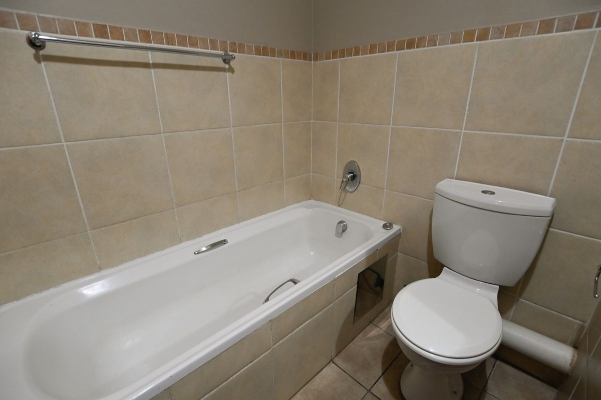 A functional bathroom featuring a standard bathtub, toilet, and neutral wall tiling with a decorative border.