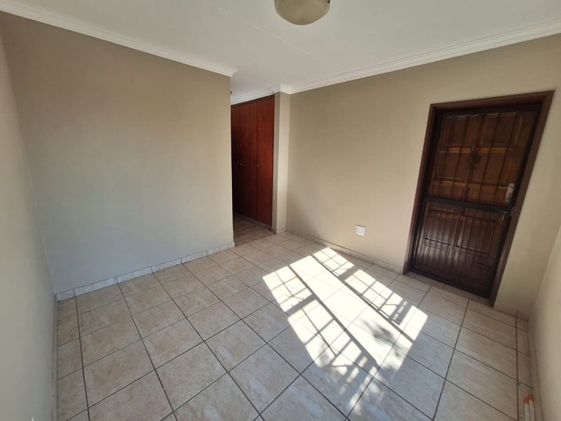 An empty bedroom featuring neutral wall tones, tiled flooring, and built-in wooden cupboards, offering a clean and versatile living space.