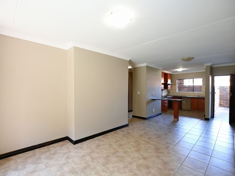 An open-plan living and kitchen area featuring tiled flooring, wooden cabinetry, a breakfast bar, and direct access to an exterior space.