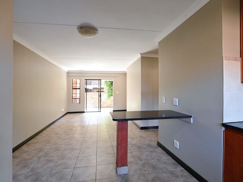 An open-plan living and kitchen area featuring tiled flooring, a breakfast bar with granite countertop, and sliding glass doors leading to the exterior.