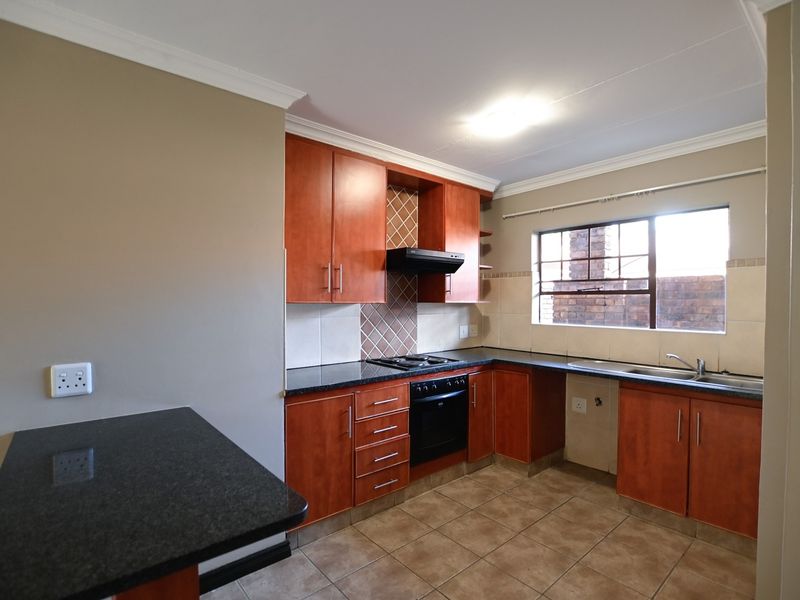 A functional kitchen featuring wooden cabinetry, granite countertops, a built-in oven with hob, extractor fan, and a double sink with tiled flooring.