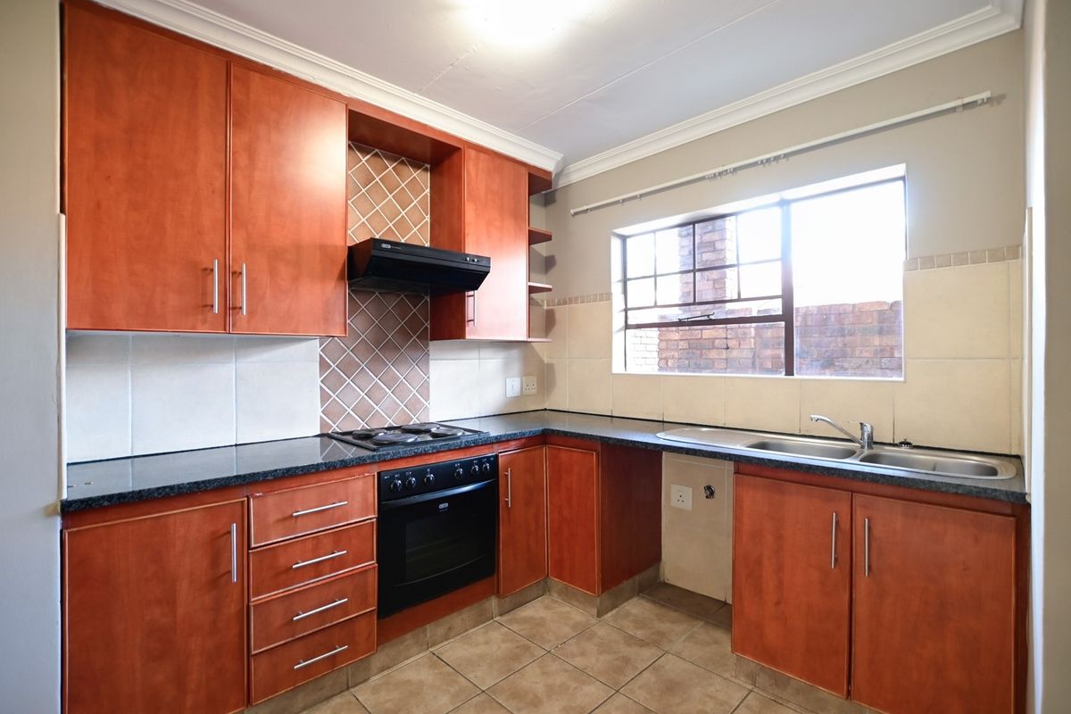 A functional kitchen featuring wooden cabinetry, granite countertops, a built-in oven with hob, extractor fan, and a double sink with tiled backsplash.