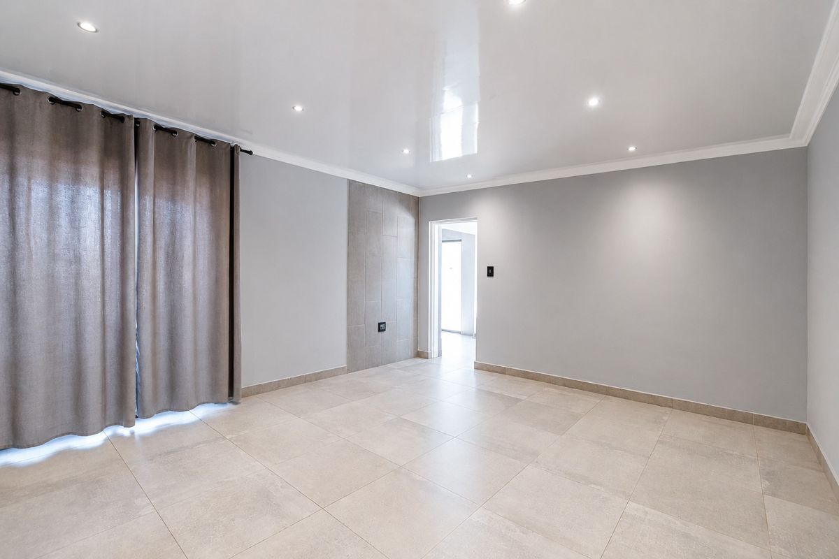 A bright, spacious, and empty living area featuring modern tiled flooring, a glossy ceiling with recessed lighting, and a neutral color palette.