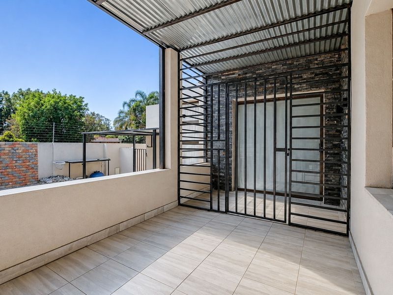 A covered patio area featuring tiled flooring, stone cladding, and a secure metal gate, providing a functional outdoor space.