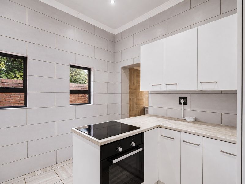 A clean, modern kitchen featuring white cabinetry, laminate countertops, a built-in oven with electric hob, and neutral wall tiling.