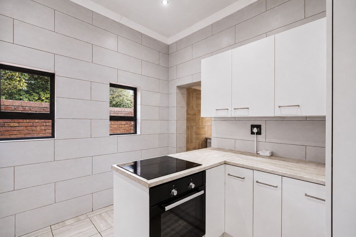 A clean, modern kitchen featuring white cabinetry, laminate countertops, a built-in oven with electric hob, and neutral wall tiling.