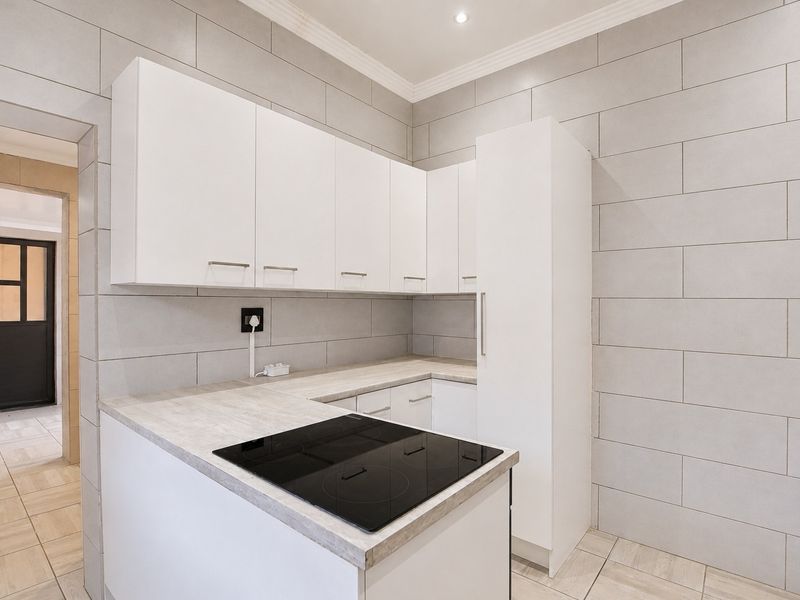 Modern kitchen featuring white cabinetry, stone-look laminate countertops, an integrated electric hob, and neutral wall tiling.