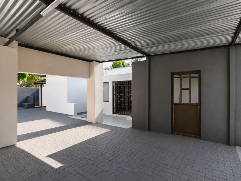 A covered carport area featuring a corrugated metal roof, paved flooring, and secure access points to the main dwelling.