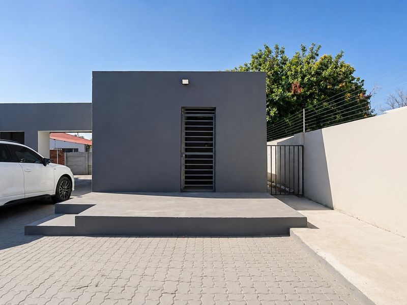 Front exterior view of the property featuring a paved driveway, concrete entrance step, and secure boundary wall with electric fencing.