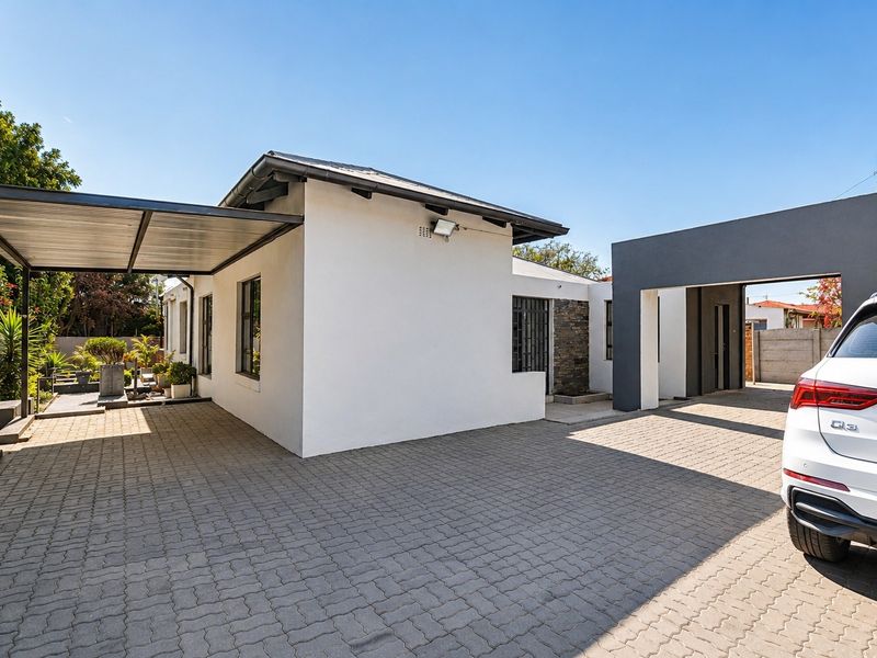 Front exterior view of the property featuring a paved driveway, covered carport, and modern stone-clad accents.