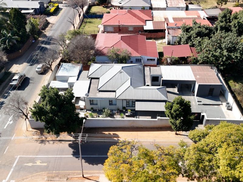 Aerial view of the property showing the main house structure, corrugated metal roofing, boundary walls, and paved driveway access from the street.