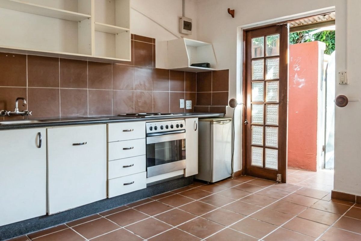 A functional kitchen featuring built-in cabinetry, a tiled backsplash, integrated oven and hob, and direct access to an outdoor area through a timber door.