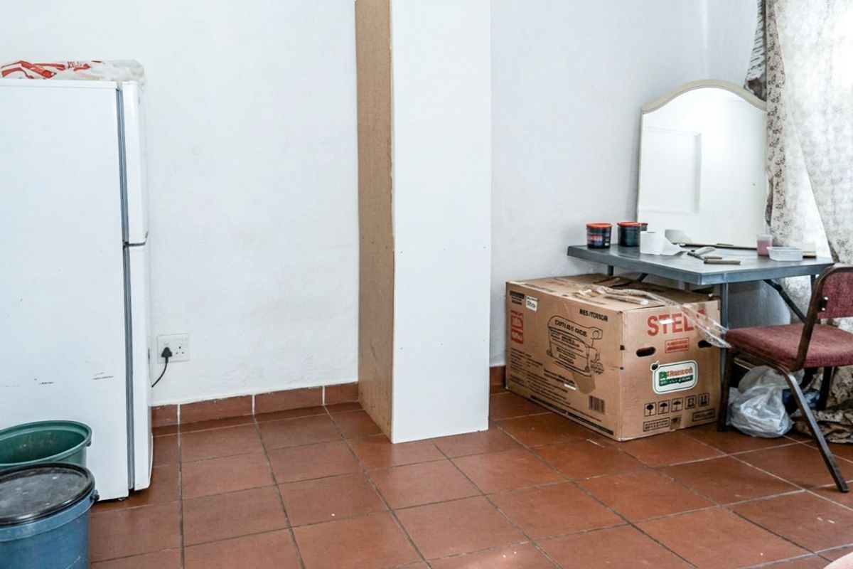 A bedroom space featuring terracotta-style floor tiles and plain white walls, currently used for storage.