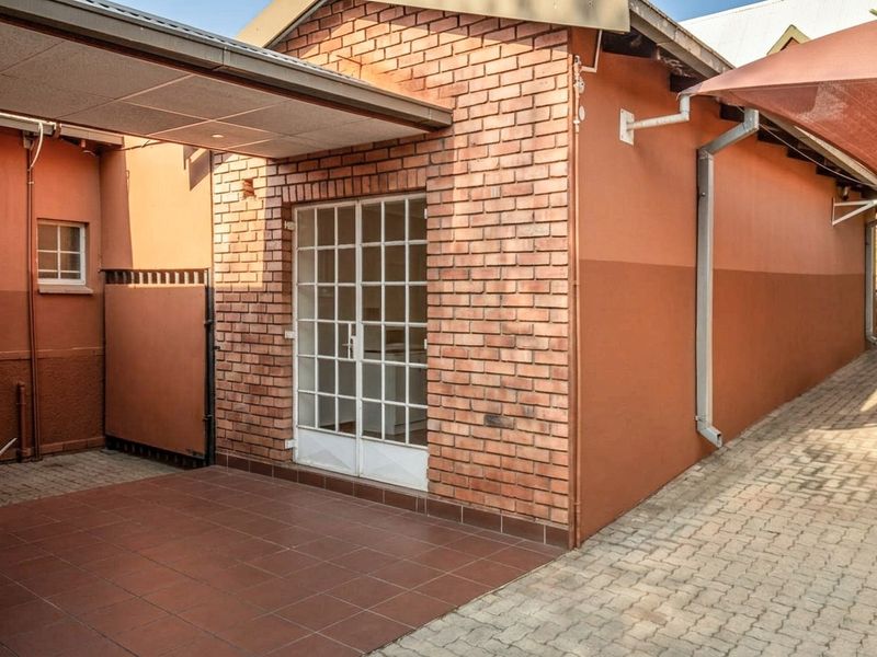 A well-maintained rear exterior area featuring a brick facade, tiled patio space, and paved walkway with functional guttering and awning.