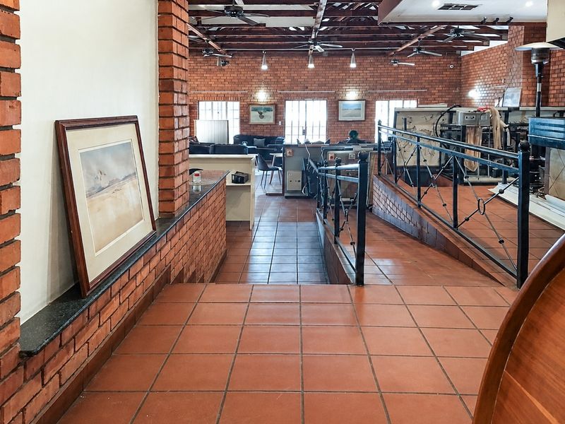 Spacious open-plan living area featuring exposed brick walls, timber beam ceilings, terracotta tiling, and a ramp for accessible navigation between levels.