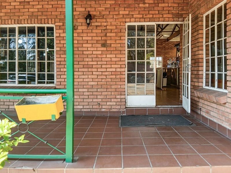 A covered patio area featuring exposed brick walls, tiled flooring, and classic grid-style windows and doors, providing a functional outdoor transition space.