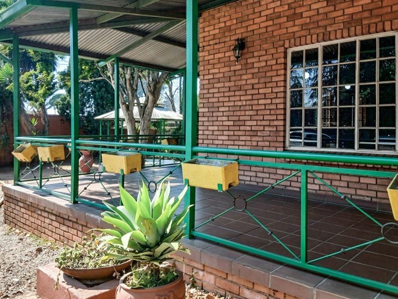 A covered outdoor patio area featuring brick wall finishes, tiled flooring, and a green metal railing structure.