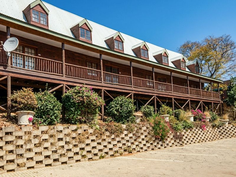 A multi-story timber-clad building featuring a long balcony, dormer windows, and a structured retaining wall overlooking a paved parking area.