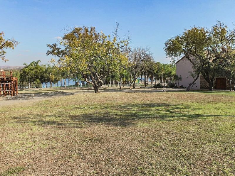 A spacious, well-maintained residential garden featuring mature trees, a wooden playground structure, and open lawn space with perimeter fencing.