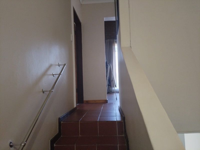 A functional staircase and hallway area featuring tiled steps and a wall-mounted metal handrail leading to an upper level landing.