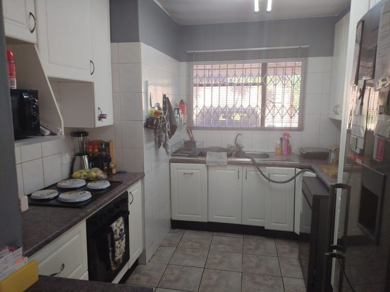 A functional kitchen featuring white cabinetry, laminate countertops, an electric hob, built-in oven, and a tiled splashback with a window overlooking the exterior.