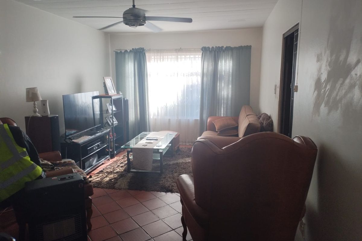 A living room featuring tiled flooring and a ceiling fan, currently showing signs of wall wear and needing cosmetic updates.