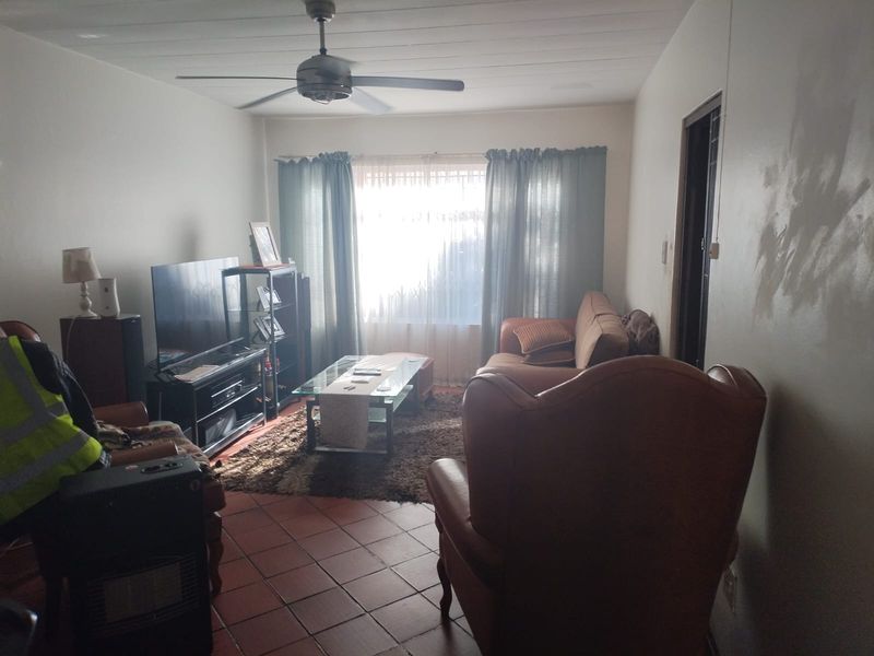 A living room featuring tiled flooring and a ceiling fan, currently showing signs of wall wear and needing cosmetic updates.
