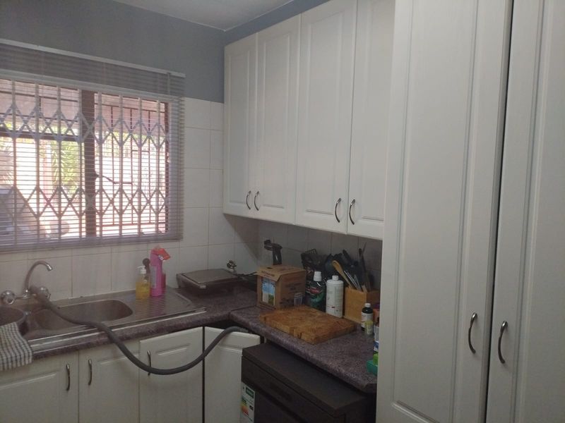 A functional scullery area featuring white built-in cabinetry, a stainless steel sink, laminate countertops, and tiled splashbacks.