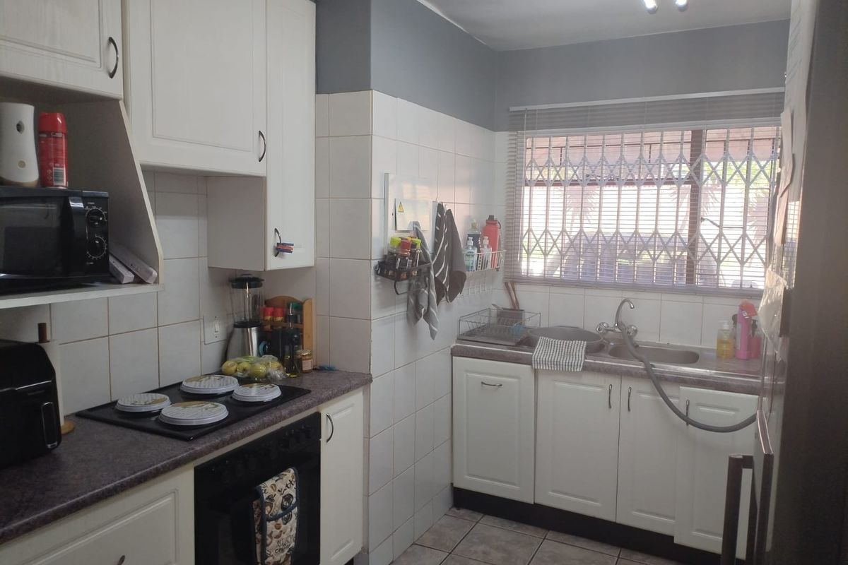 Functional kitchen featuring white cabinetry, laminate countertops, built-in oven and hob, tiled backsplash, and a window with security bars.