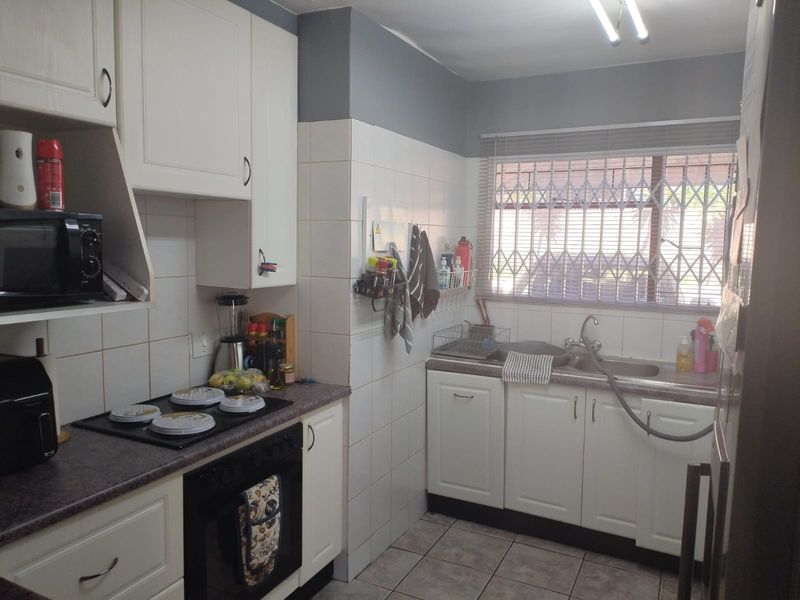 Functional kitchen featuring white cabinetry, laminate countertops, built-in oven and hob, tiled backsplash, and a window with security bars.