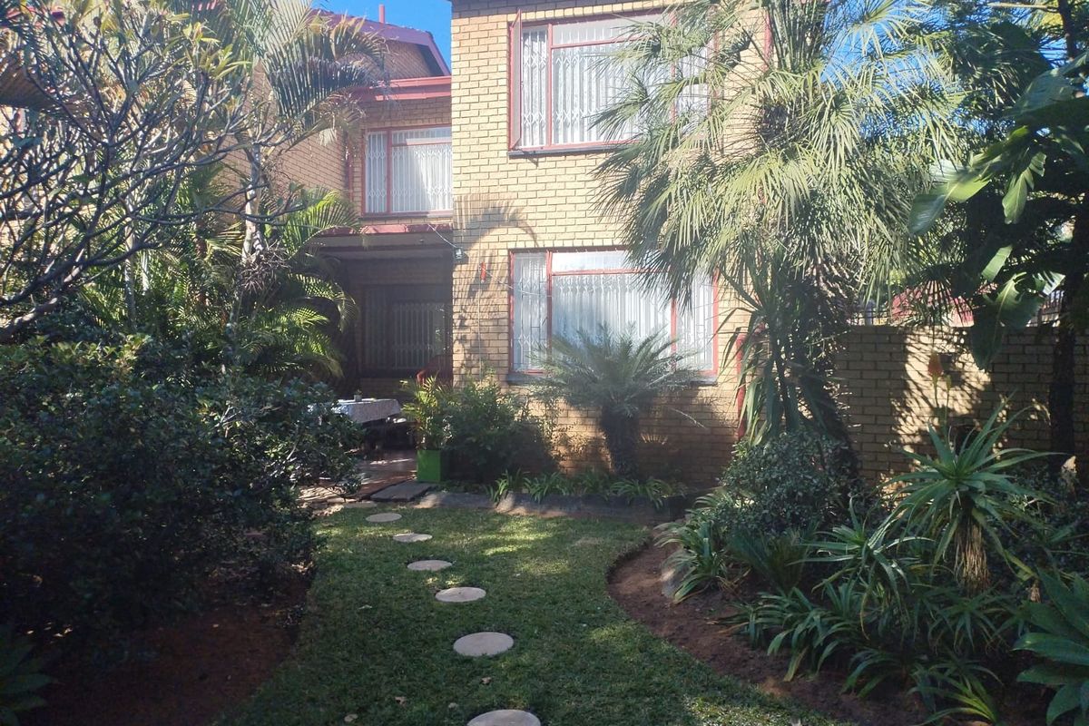 Rear view of a double-story face brick townhouse featuring a landscaped garden, paved stepping stone path, and established greenery.