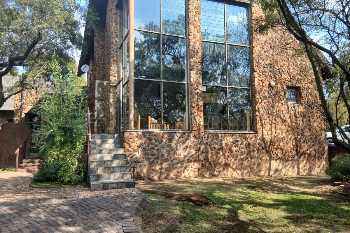 Rear elevation of a stone-clad residence featuring expansive floor-to-ceiling windows, a stone staircase, and a paved walkway set within a landscaped garden.