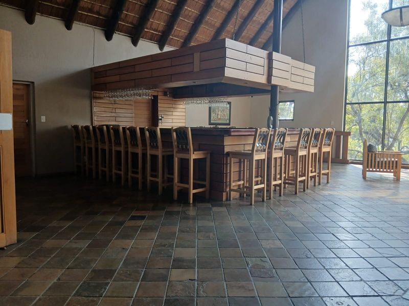 Spacious bar area featuring a large built-in timber counter, suspended canopy, tiled flooring, and high thatched ceilings with expansive windows overlooking the landscape.