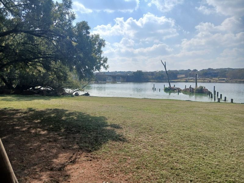 A scenic view of the waterfront featuring a grassy lawn, mature trees, and a distant bridge, highlighting the natural landscape of the property.