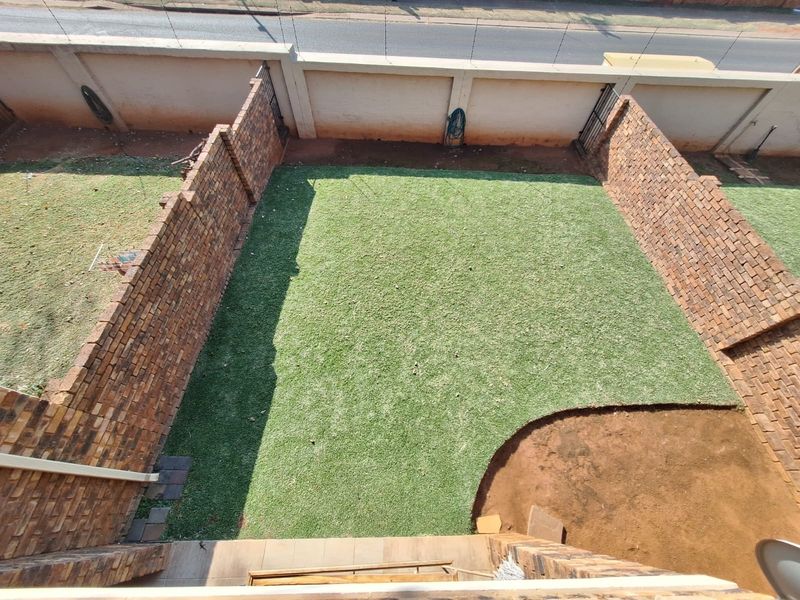 An elevated view of a private rear garden featuring brick boundary walls and a lawn area with some unfinished landscaping.