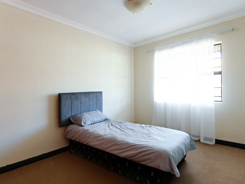 A simple bedroom featuring neutral walls, carpet flooring, and a window fitted with security bars.