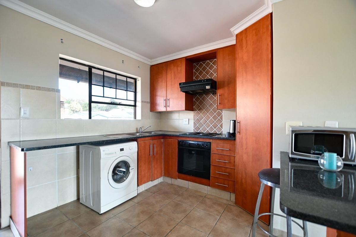 Functional kitchen featuring wood-finish cabinetry, granite countertops, built-in oven, hob, extractor fan, and tiled flooring with space for a washing machine.