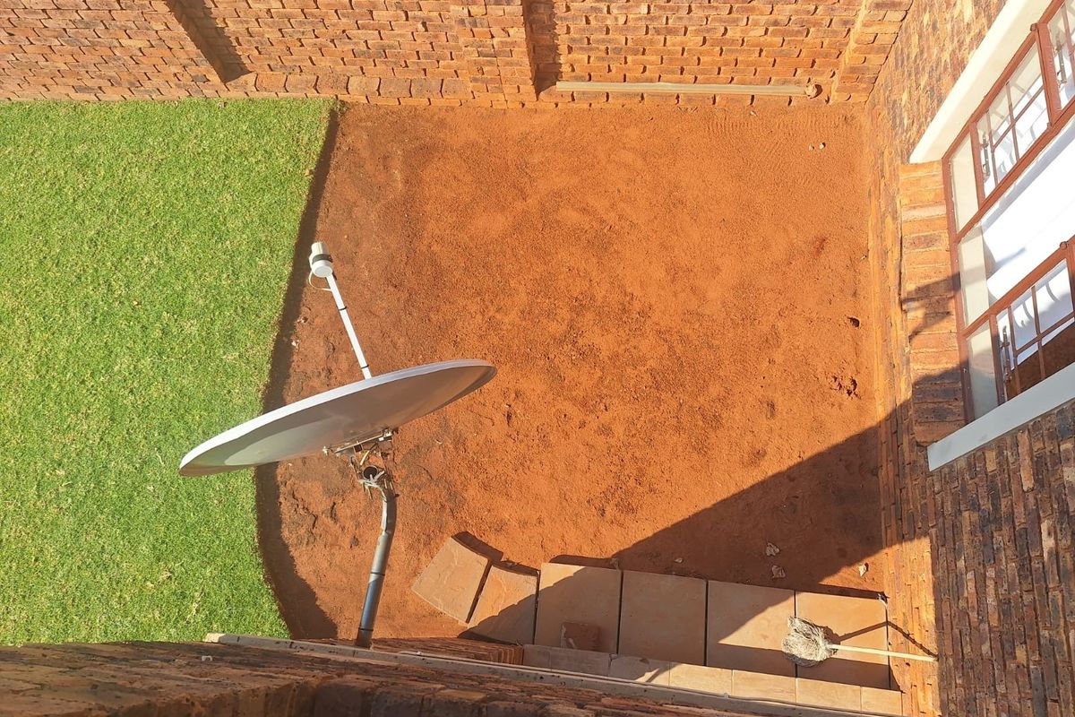 An elevated view of a rear garden featuring a brick boundary wall, a small paved patio section, and an unlandscaped soil area.