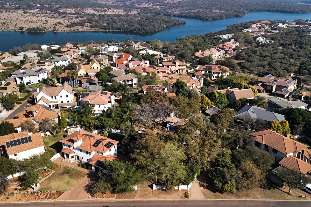 An aerial view of a residential estate featuring multiple homes with tiled roofs, solar panels, and mature landscaping near a large body of water.