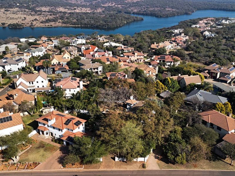 An aerial view of a residential estate featuring multiple homes with tiled roofs, solar panels, and mature landscaping near a large body of water.