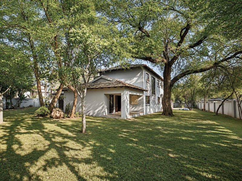 A view of the rear elevation of the house featuring a covered patio, established trees, and a spacious garden enclosed by a perimeter wall.