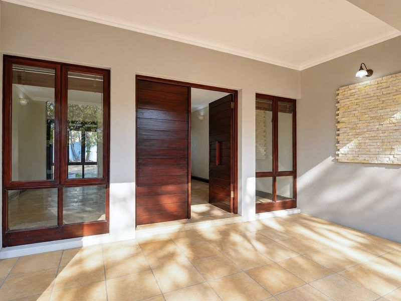 A covered patio area featuring tiled flooring, timber-framed glass doors, and a decorative stone-clad feature wall with integrated lighting.
