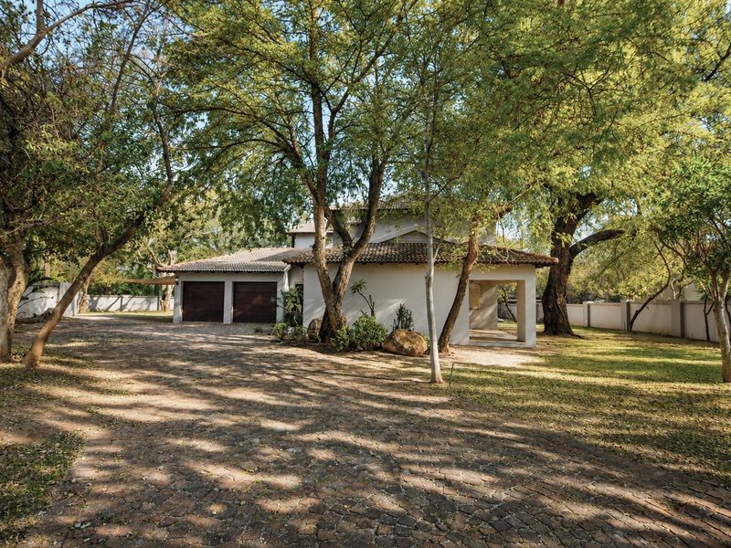 Front view of a residential property featuring a double garage, paved driveway, and mature trees set within a landscaped garden.
