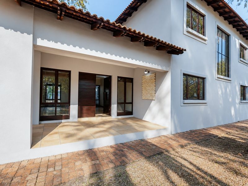 A covered patio area featuring tiled flooring, timber door frames, and a stone feature wall, leading to a brick-paved exterior walkway.