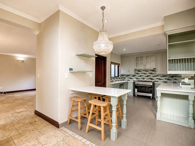 A well-appointed kitchen featuring sage green cabinetry, stone countertops, a gas stove, and a breakfast bar area with pendant lighting.