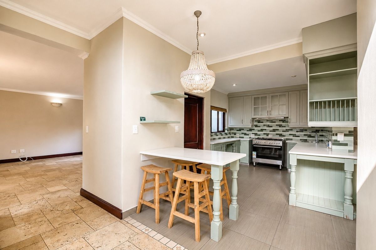 A well-appointed kitchen featuring sage green cabinetry, stone countertops, a gas stove, and a breakfast bar area with pendant lighting.