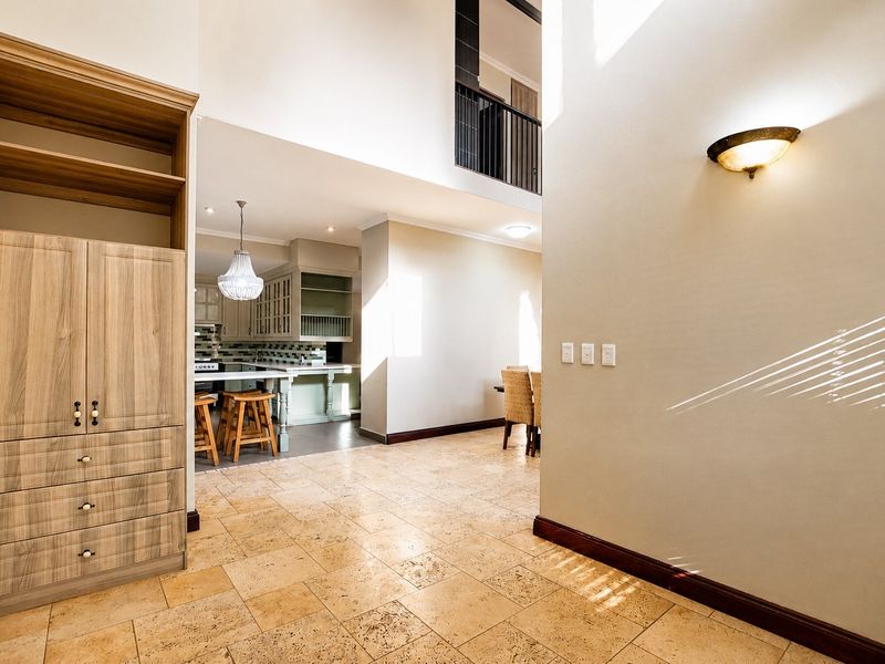Spacious open-plan living area featuring travertine tile flooring, high ceilings with a mezzanine level, and a well-appointed kitchen with built-in cabinetry.
