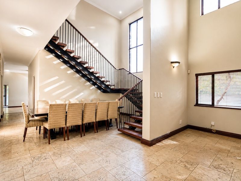 Spacious open-plan dining area featuring high ceilings, large windows for natural light, and a striking open-tread staircase with metal balustrades.