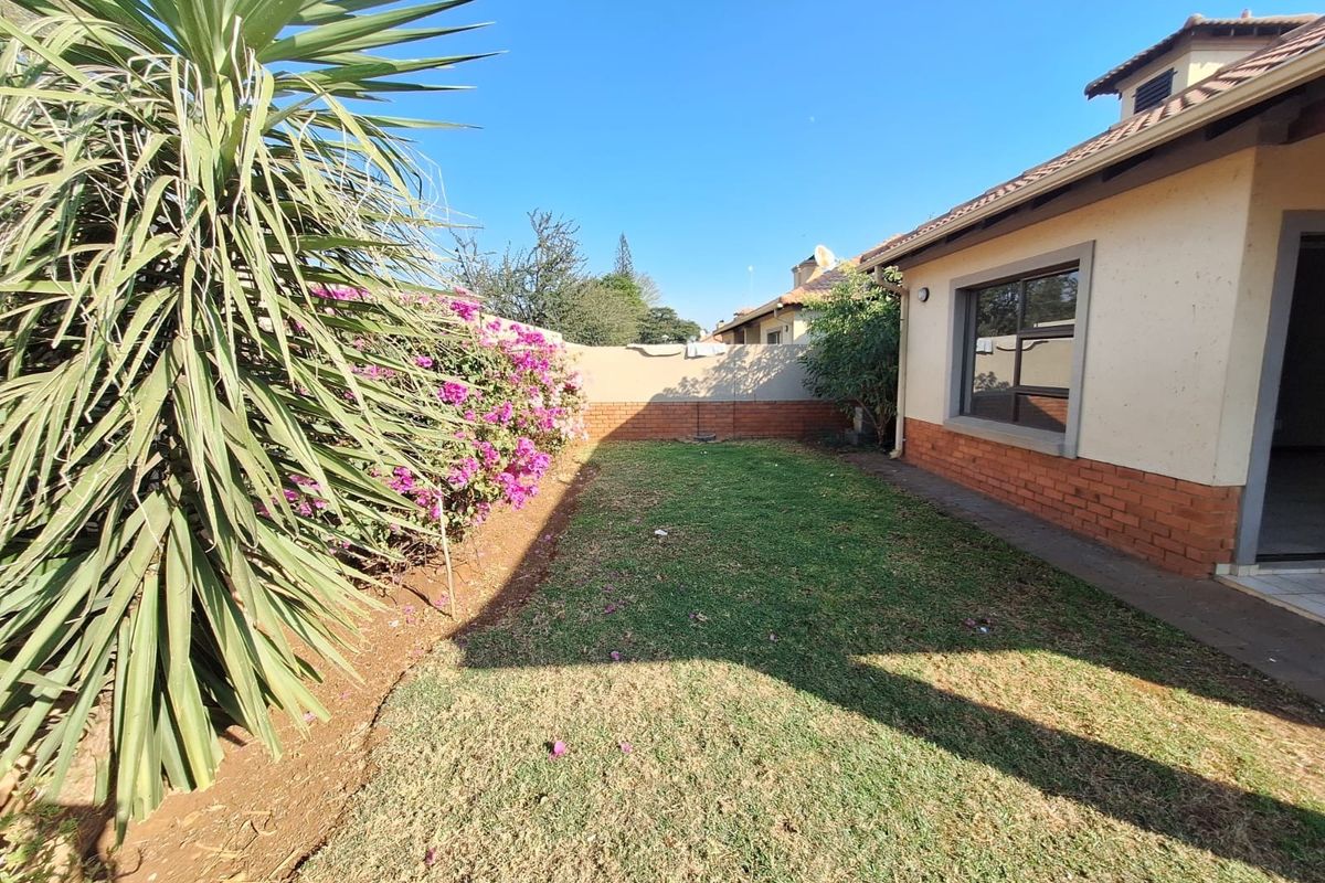 A private rear garden area featuring a lawn, established landscaping, and a brick boundary wall, adjacent to the townhouse structure.